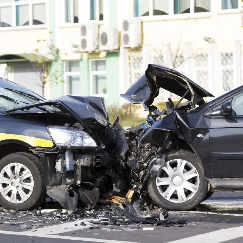 Head-on collision between two vehicles, showing significant front-end damage, debris scattered on the road, and a city backdrop, highlighting the dangers of vehicle collisions in high-traffic areas.