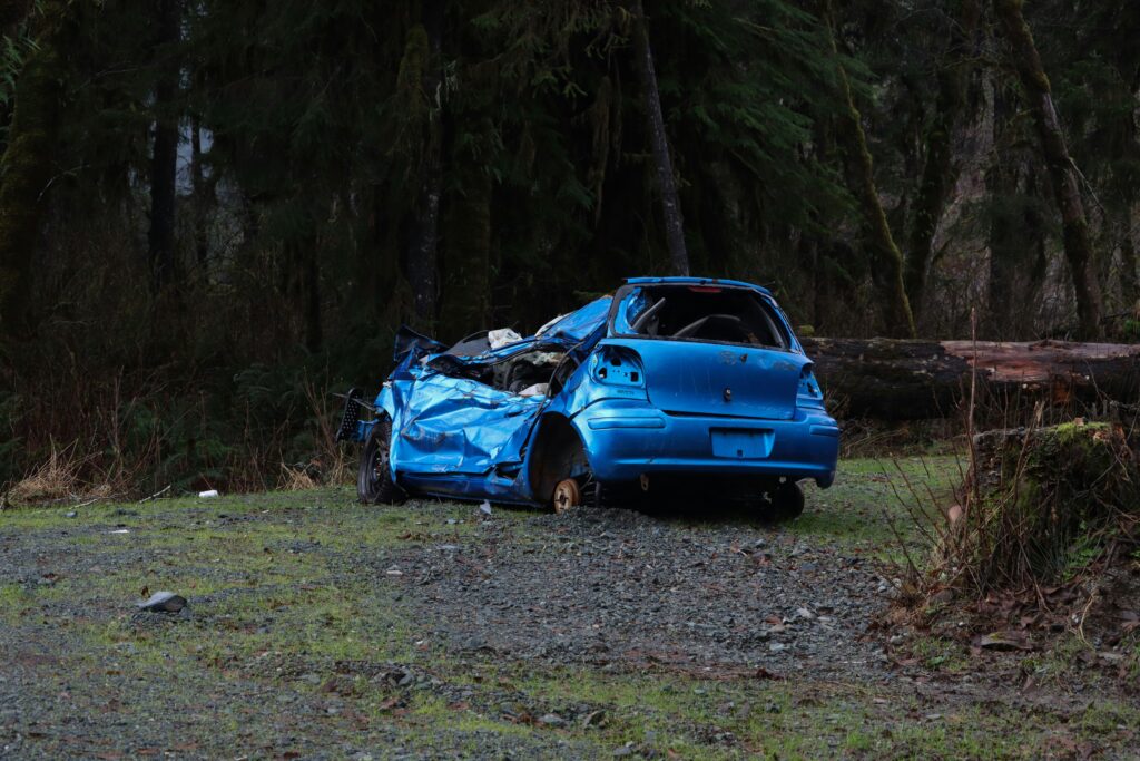 Damaged blue car wreck in a forested area, illustrating the aftermath of a vehicle collision relevant to personal injury cases and legal assistance in Spring, Texas.