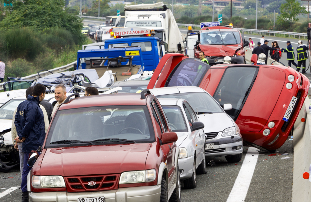 Multi-vehicle accident scene on a highway with overturned red car, damaged vehicles, and emergency responders discussing the incident.
