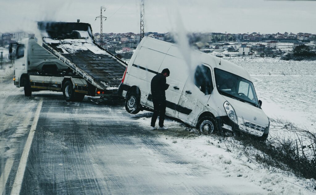 Van stuck in snow beside a tow truck on a road, emphasizing vehicle collisions and accidents in winter conditions relevant to personal injury claims in Clear Lake.