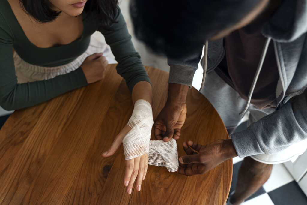Person assisting another with a bandaged hand at a wooden table, highlighting the theme of injury care relevant to personal injury law services near Love Field.