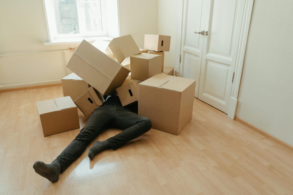 Person lying on the floor under a pile of cardboard boxes in an indoor setting, illustrating potential slip and fall hazards in residential areas.