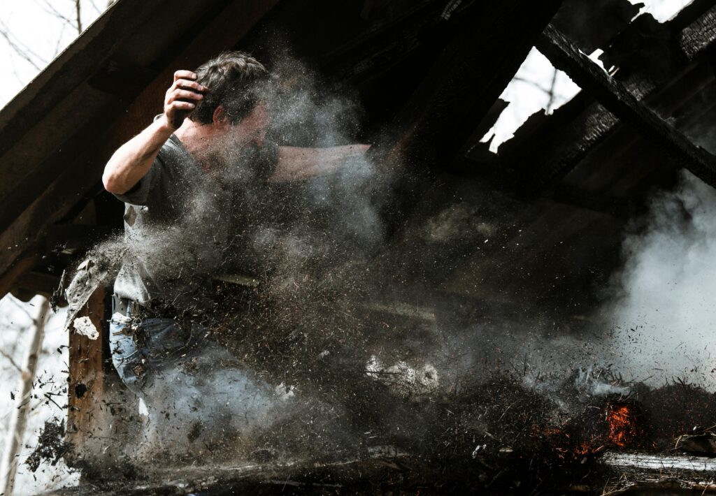 Man working on a damaged roof, surrounded by debris and smoke, highlighting the risks of personal injury in construction or renovation settings.