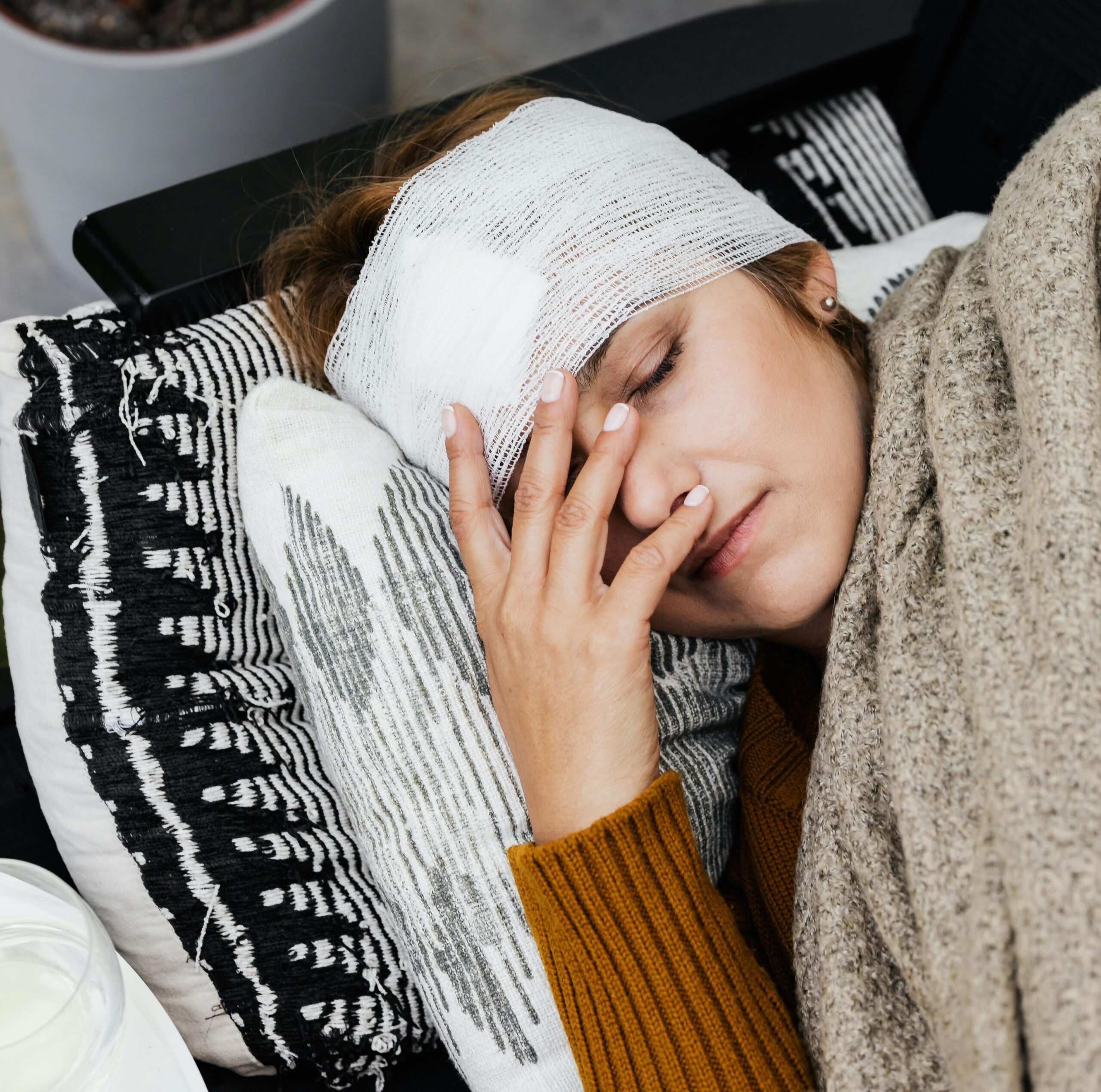 Woman with a head injury resting on pillows, showing signs of distress, emphasizing the impact of personal injuries from accidents.