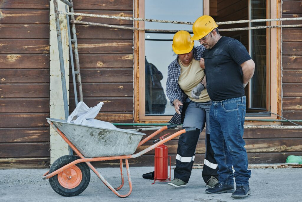 Construction workers in hard hats discussing safety measures near a wheelbarrow and fire extinguisher, emphasizing the importance of safety in personal injury cases.