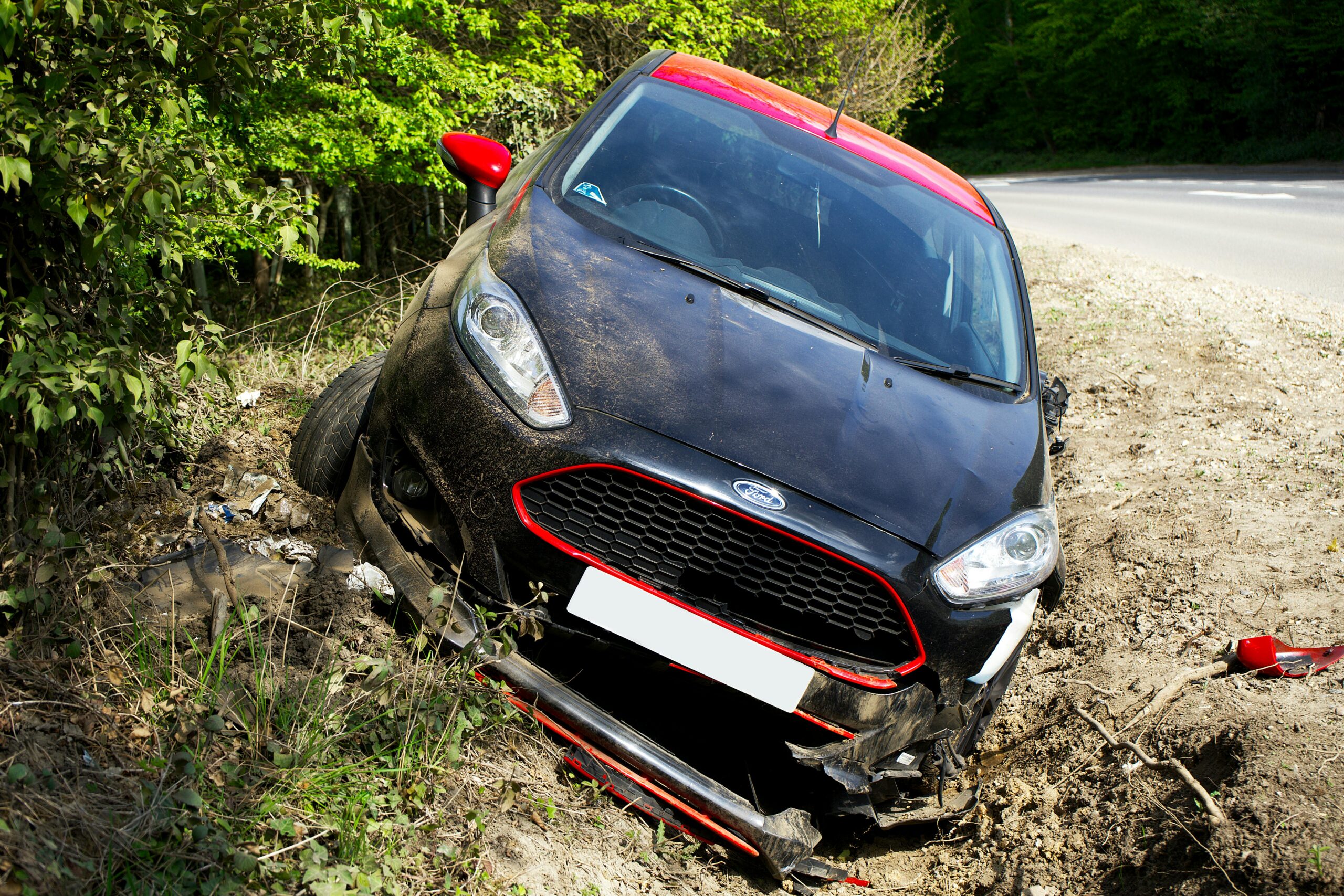 Black Ford Fiesta car in a ditch, showing signs of a car accident, surrounded by greenery and dirt, relevant to personal injury cases in Healy-Murphy.