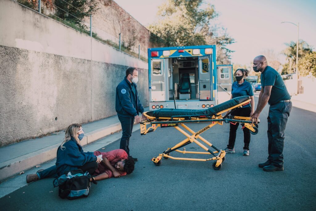 Emergency medical personnel assisting an injured individual on the street, preparing a stretcher near an ambulance, highlighting urgent care and accident response relevant to personal injury cases in Dallas.