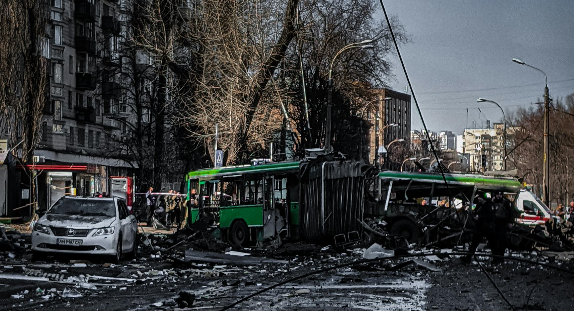 Destruction at urban accident scene with overturned green bus, damaged white car, debris, and emergency responders in the Design District, highlighting personal injury risks.