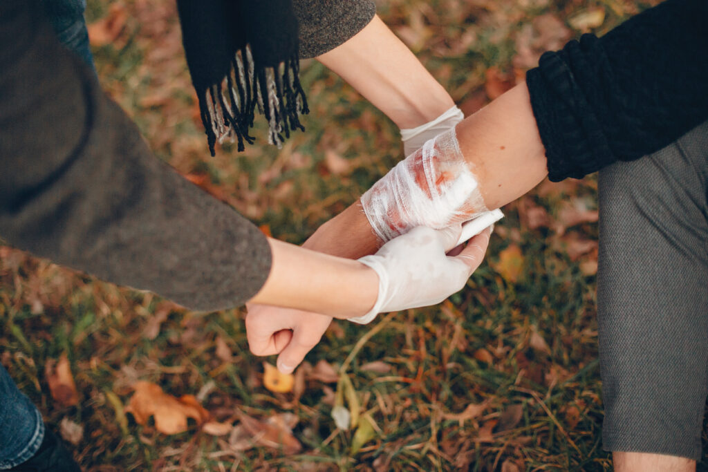 Person providing first aid by bandaging an injured arm in a park setting, emphasizing personal injury care and support.