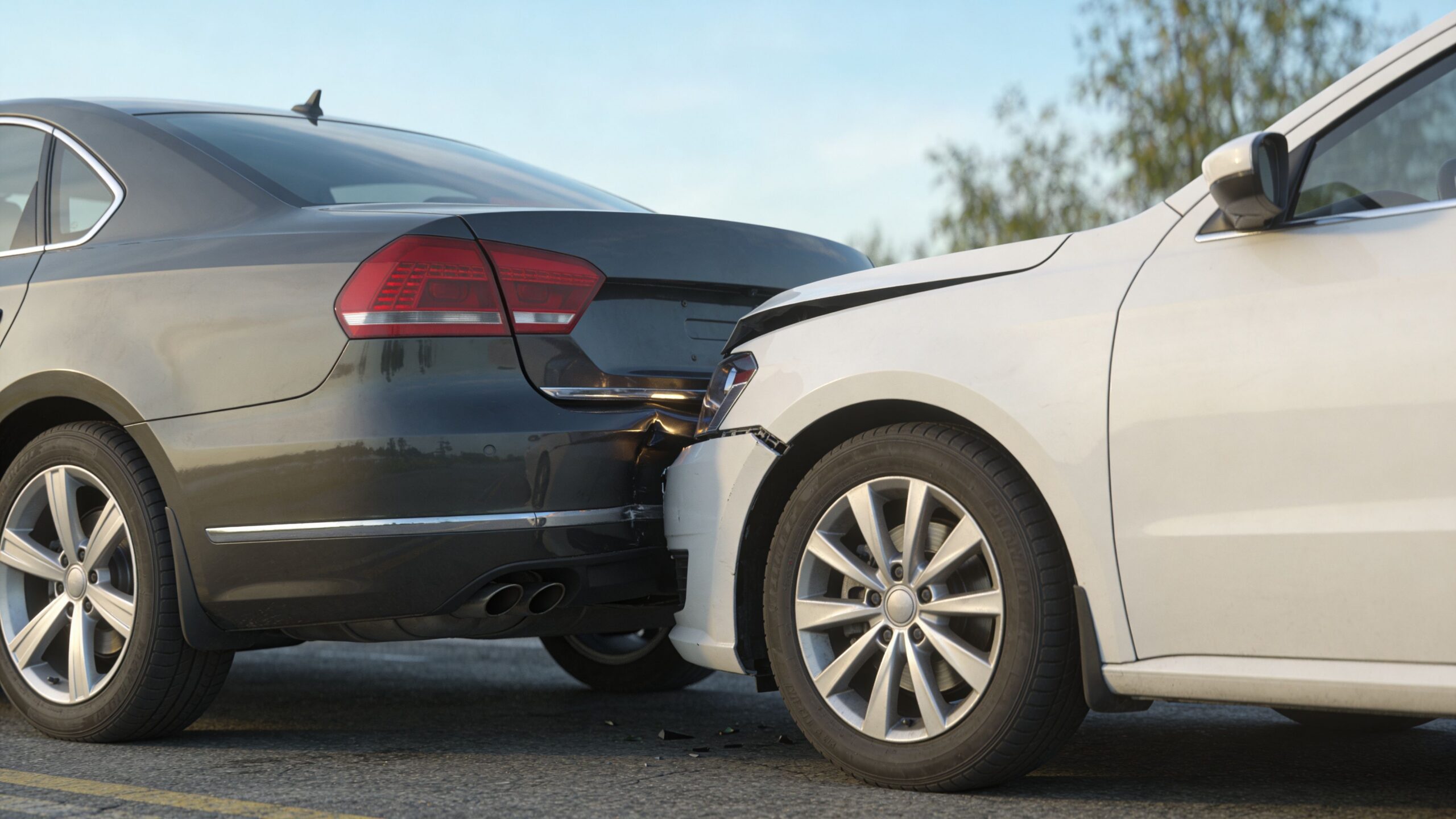 A gray and a white car involved in a rear end collision on a paved road surface.