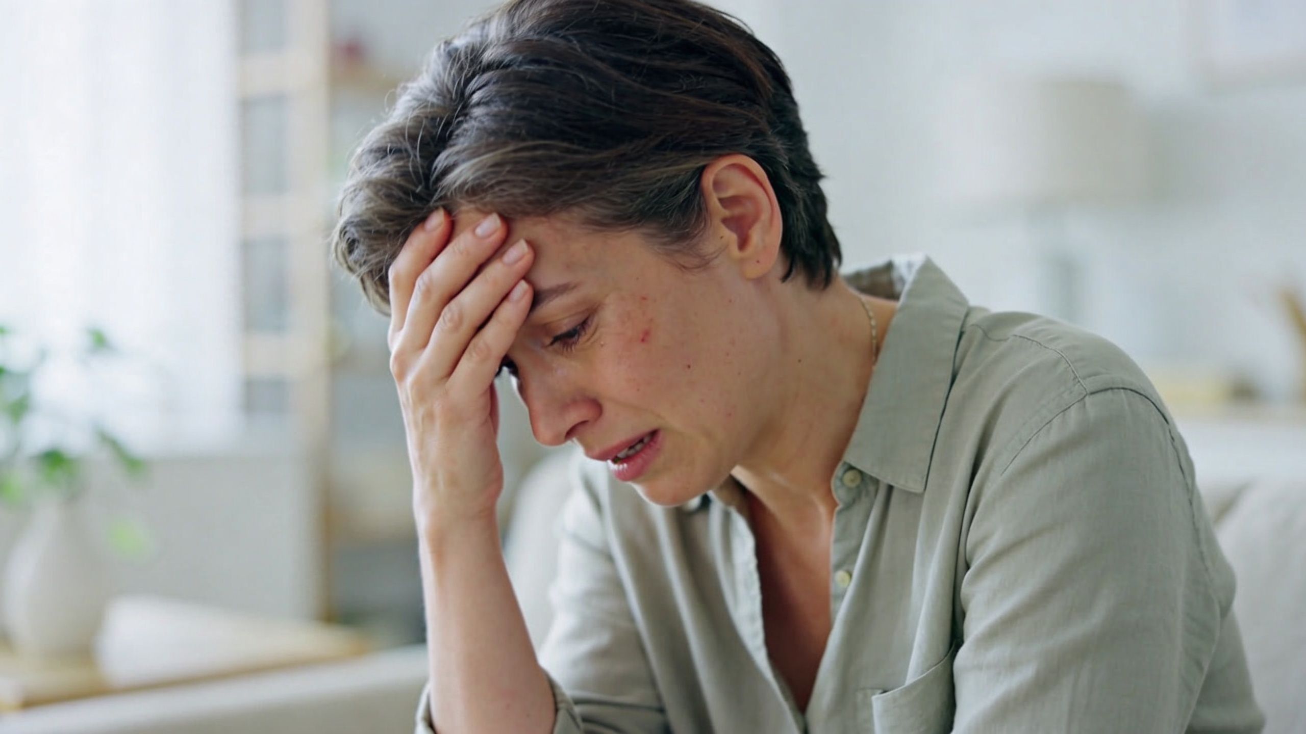 A distressed woman holding her head and crying while experiencing emotional pain at home.
