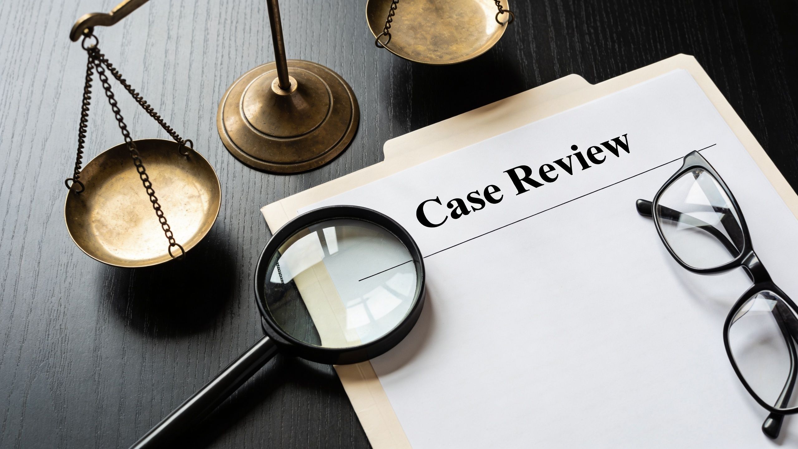 A close-up view of legal scales, magnifying glass, and glasses on a Case Review document.