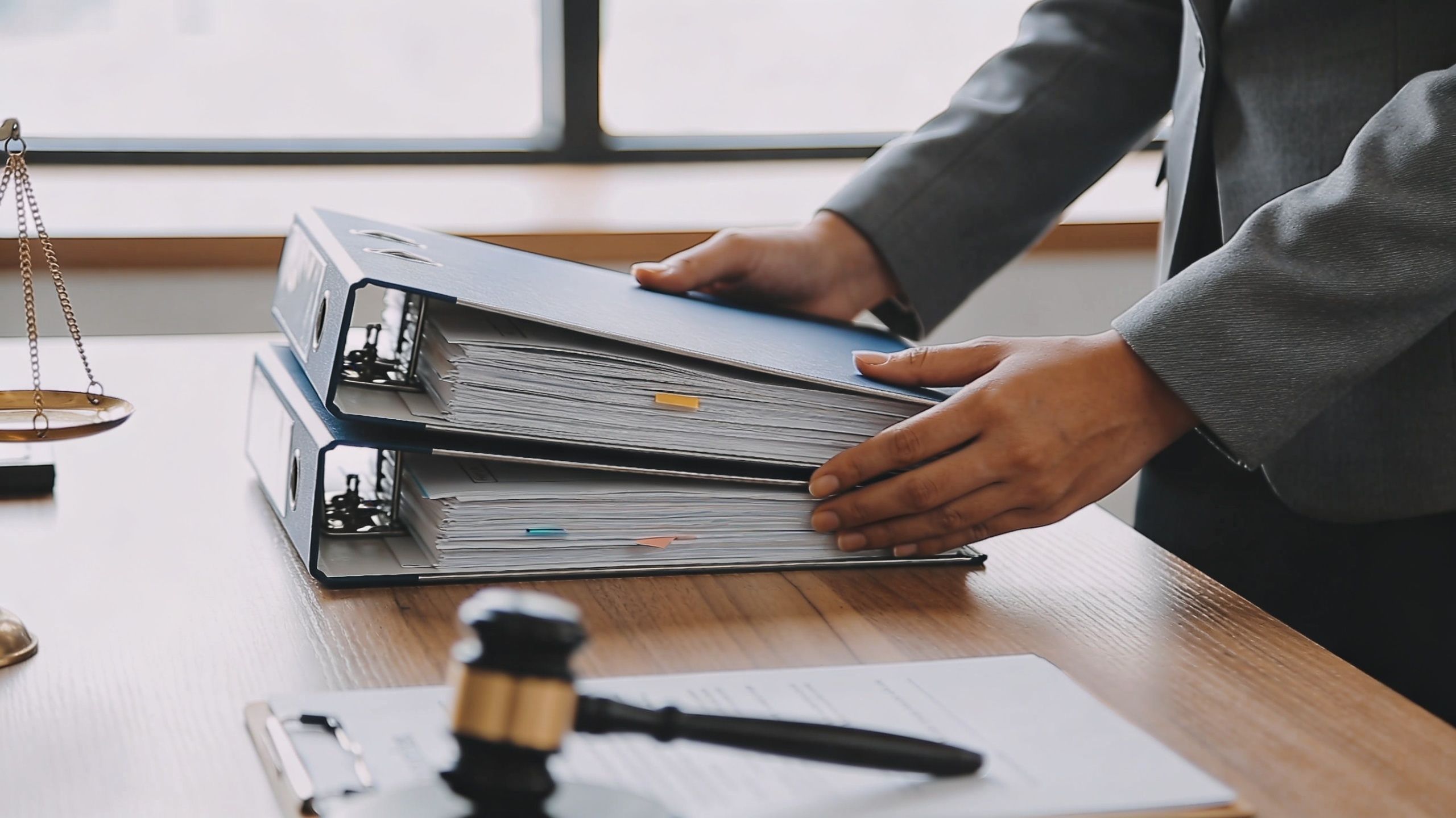 A lawyer organizing document binders on a wooden desk with a judge's gavel and scales of justice.